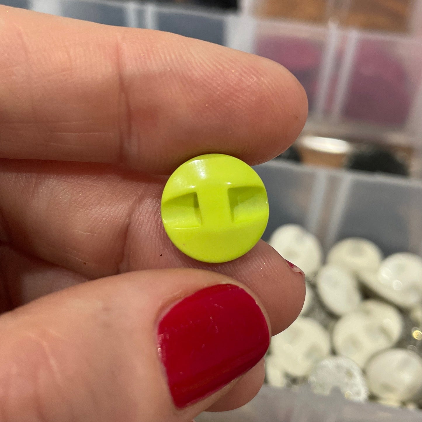 Hand holding a yellow button with a blurred background of button containers.