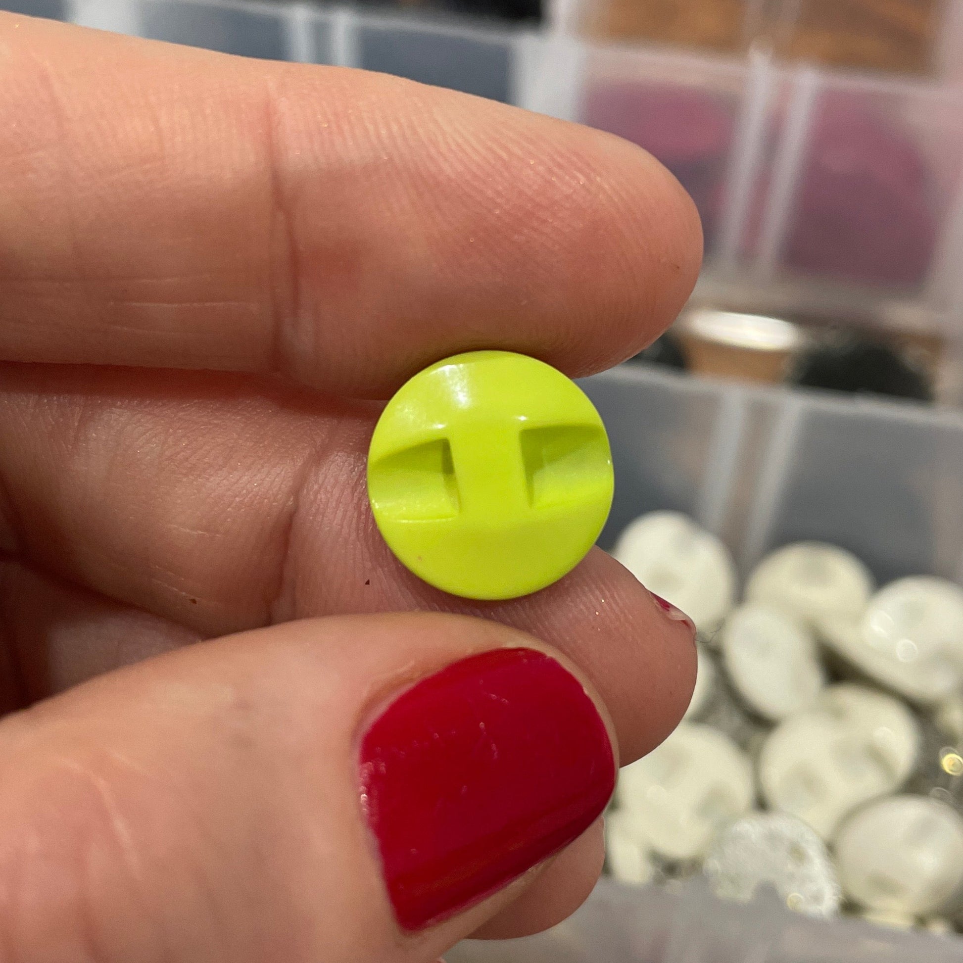 Hand holding a yellow button with a blurred background of button containers.
