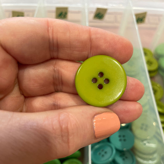 Green button held between fingers with a container of buttons in the background