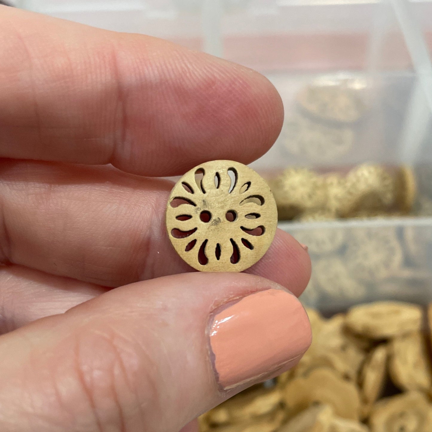 Gold button held by a hand with a container of buttons in the background