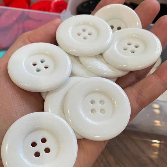 Hand holding white buttons with a clear container of buttons in the background