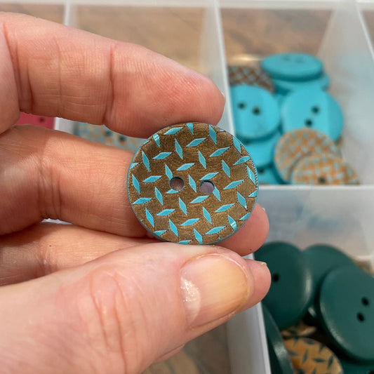 Hand holding a patterned button with a container of buttons in the background