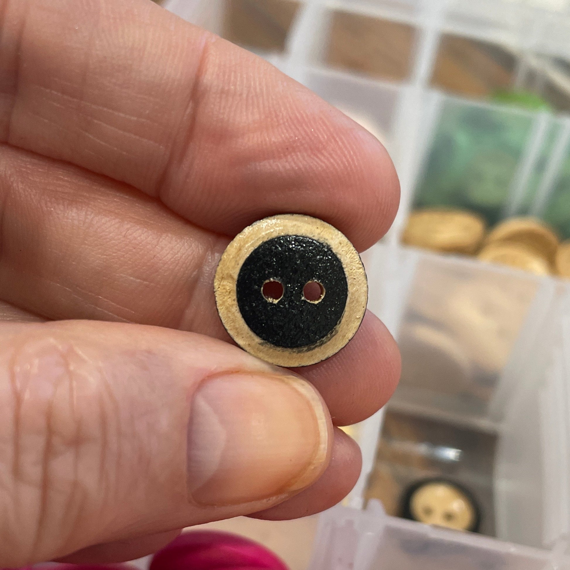 Hand holding a button with a container of various buttons in the background