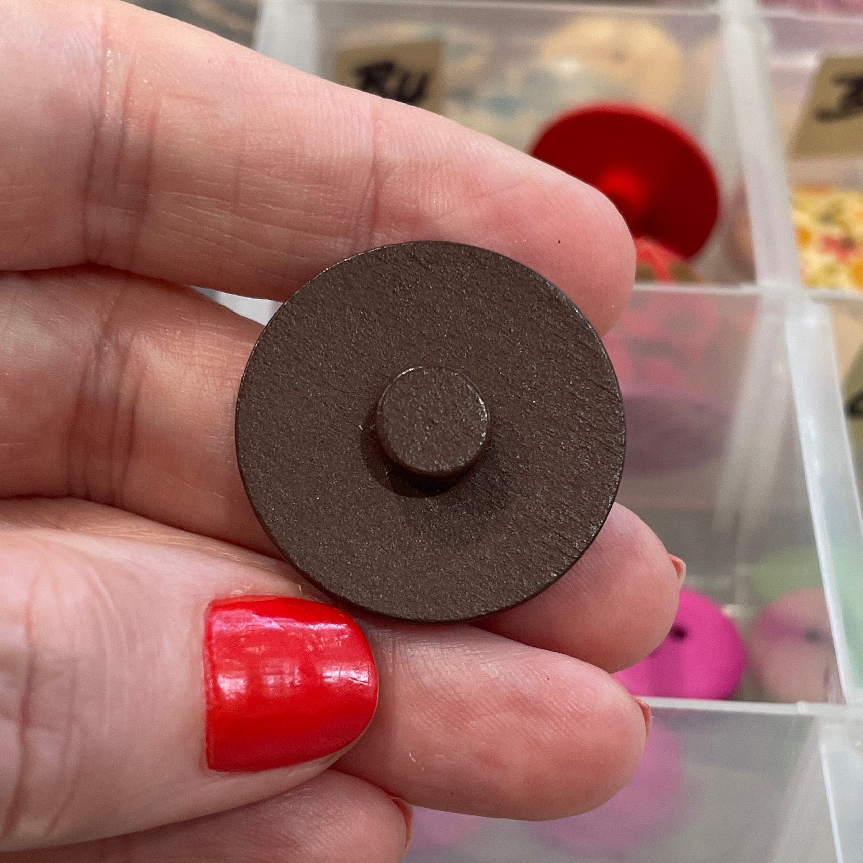 Hand holding a round button with a colorful button collection in the background