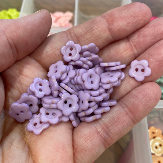 Hand holding small purple flower-shaped beads with a blurred background of more beads.