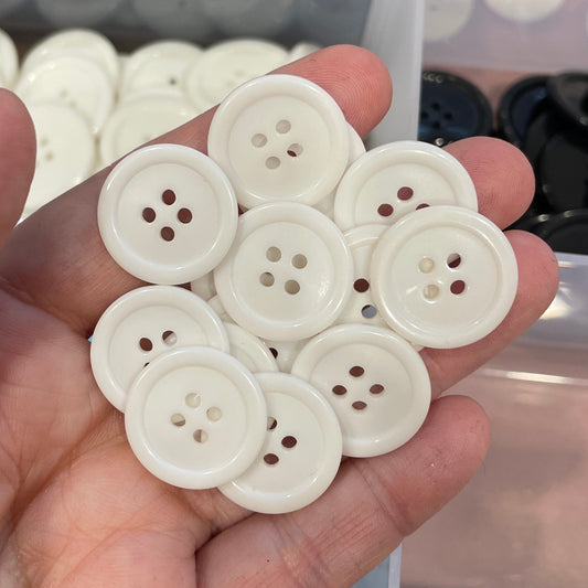 Hand holding white buttons with a container of black buttons in the background