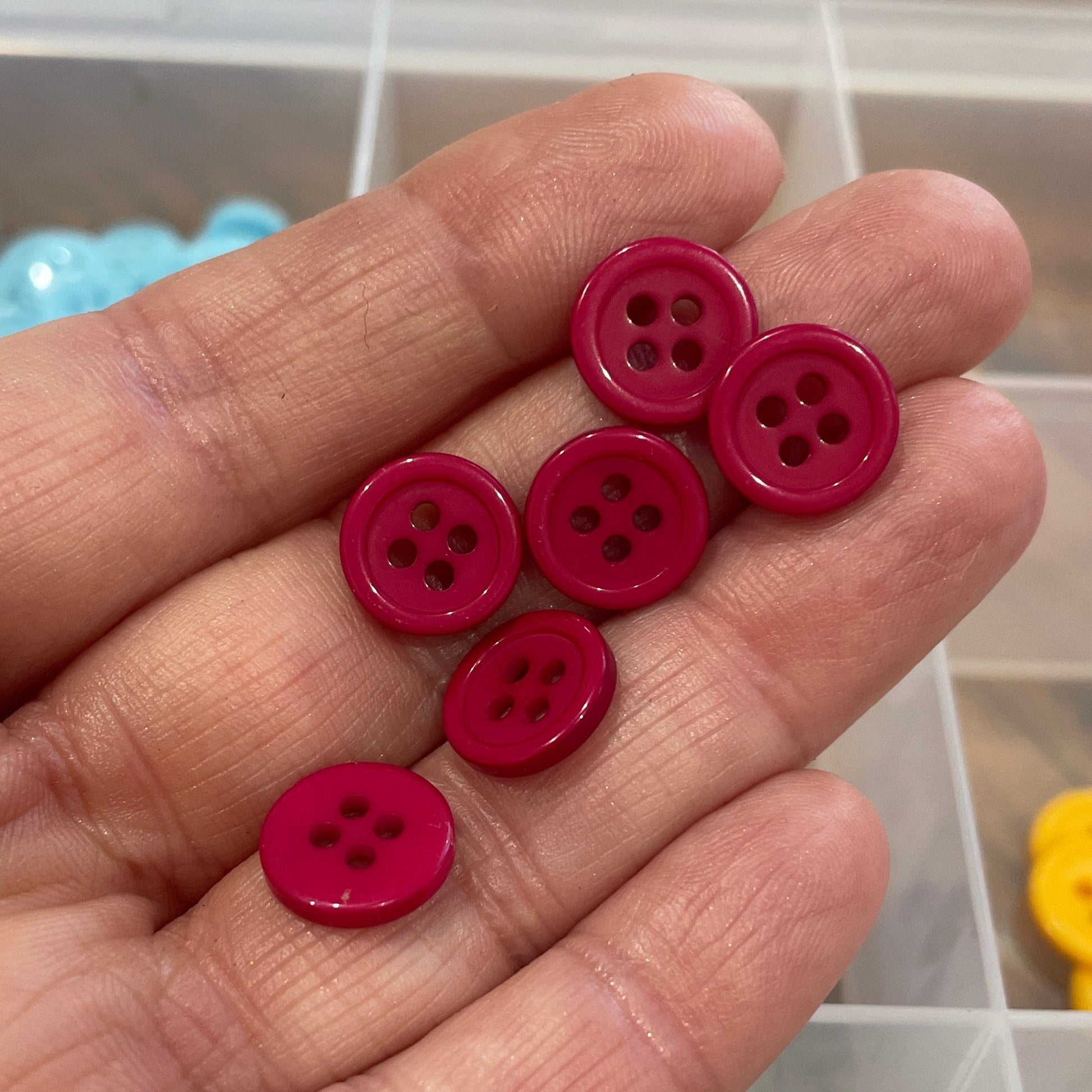 Hand holding red buttons with a background of colorful buttons in a container