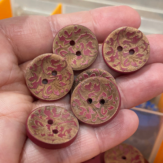 Hand holding decorative buttons with a container of more buttons in the background