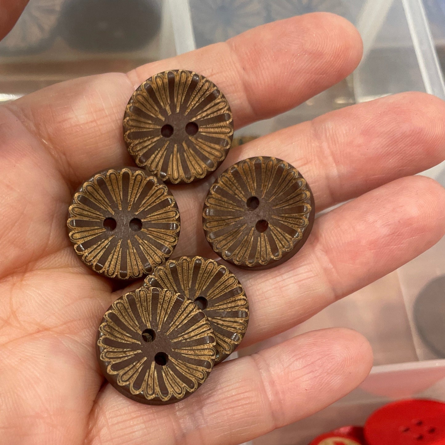 Hand holding bronze buttons with a container of various buttons in the background