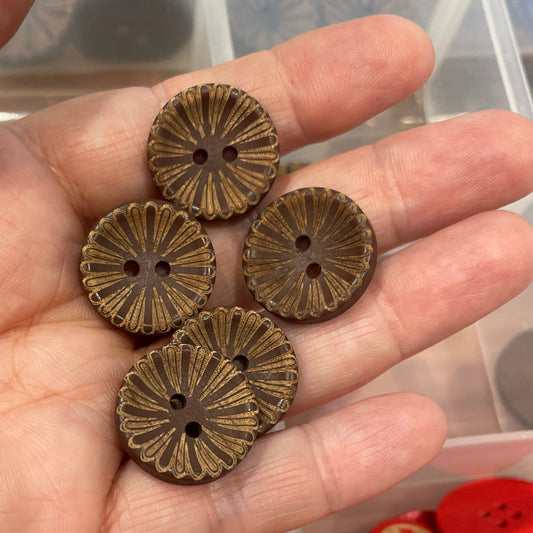 Hand holding bronze buttons with a container of various buttons in the background