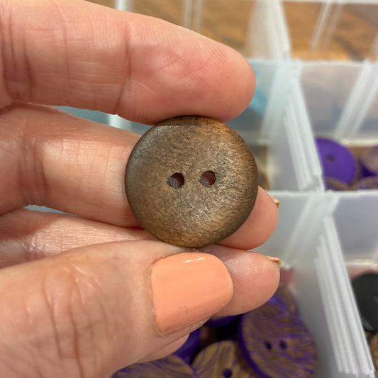 Hand holding a small brown button with a clear container of buttons in the background