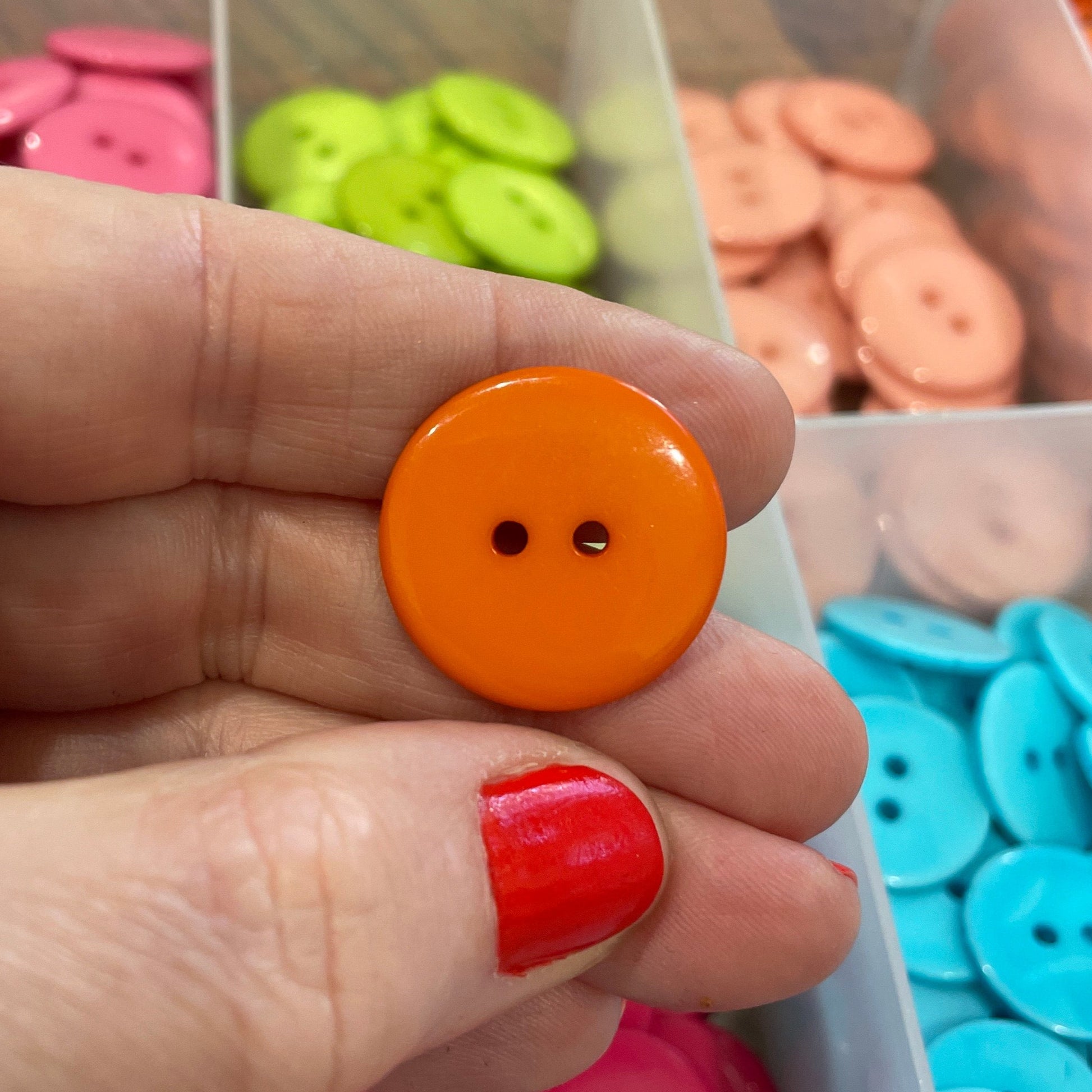 Hand holding an orange button with a background of colorful buttons in a box.