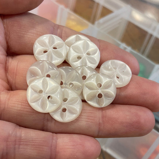 Hand holding decorative buttons with a container of similar buttons in the background