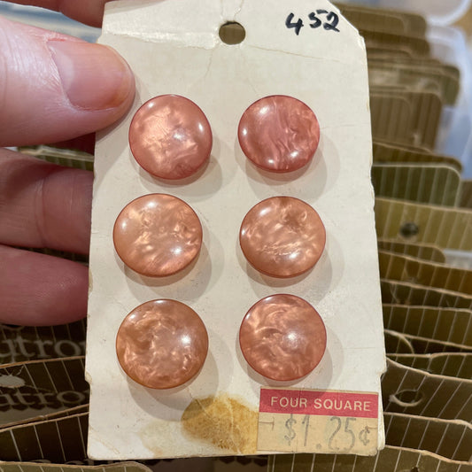 Packaged pink buttons held by a hand with a clear container in the background