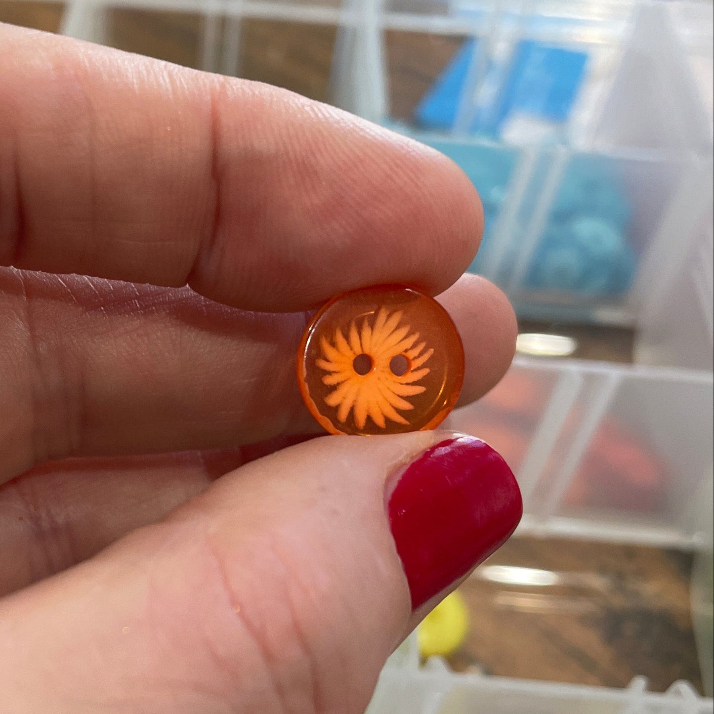 Hand holding a small orange object with a sun design against a blurred background of shelves.