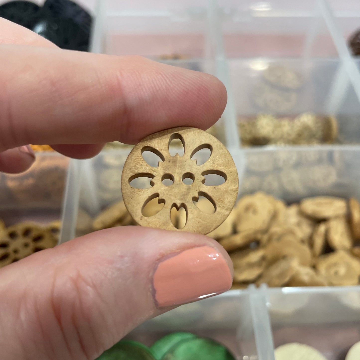 Hand holding a gold button with intricate design, surrounded by various buttons in a clear container.