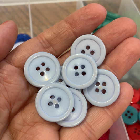 Hand holding white buttons with a container of colorful buttons in the background