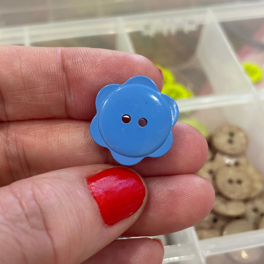 Hand holding a blue button with a flower design in front of a container of buttons.