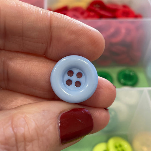 Hand holding a white button with four holes in front of a colorful button collection.