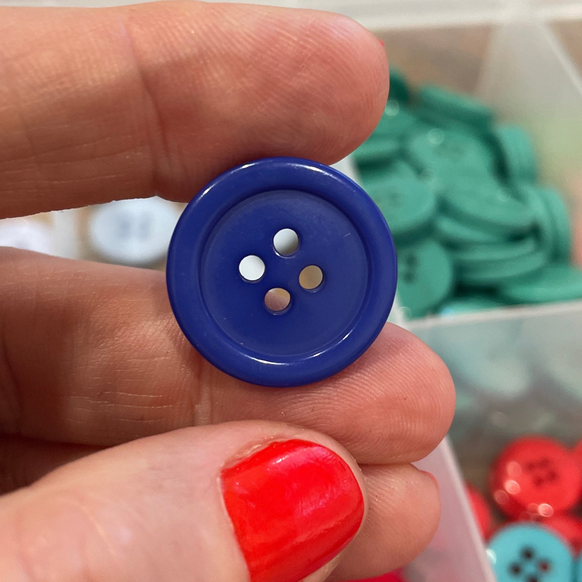 Hand holding a blue button with a container of colorful buttons in the background