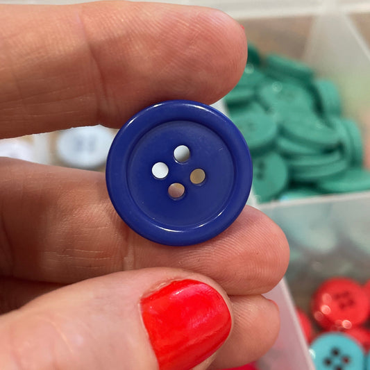 Hand holding a blue button with a container of colorful buttons in the background