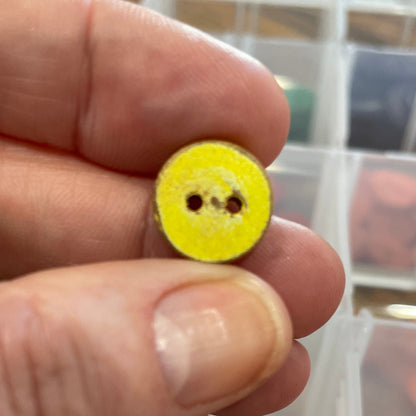 Hand holding a yellow button with a clear container of buttons in the background