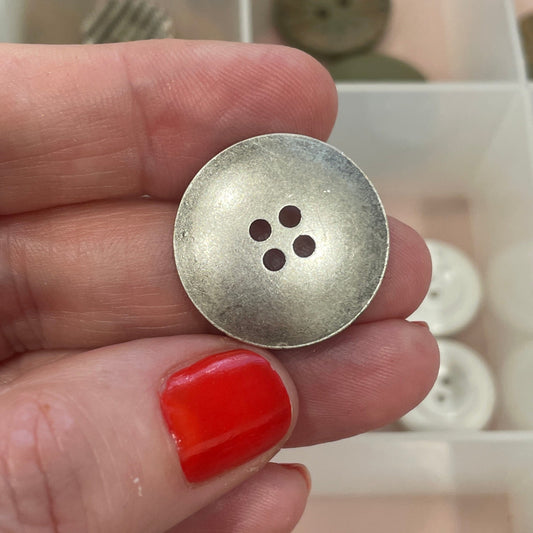 Hand holding a silver button with a blurred background of button collection