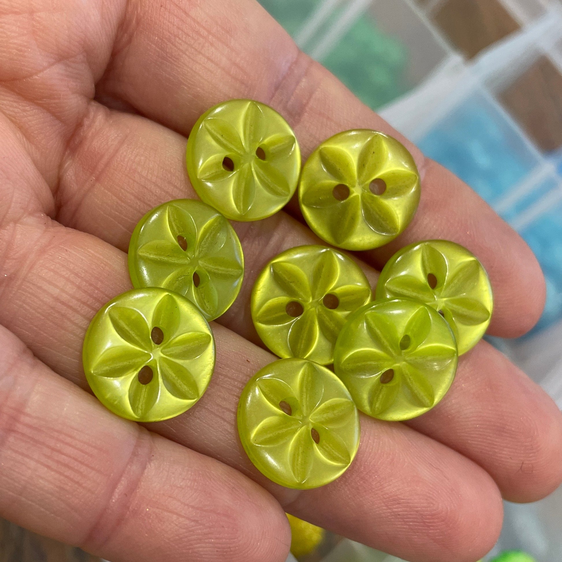 Hand holding yellow buttons with a blurred container of green buttons in the background