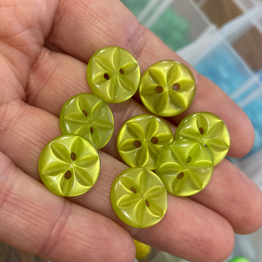 Hand holding yellow buttons with a blurred container of green buttons in the background