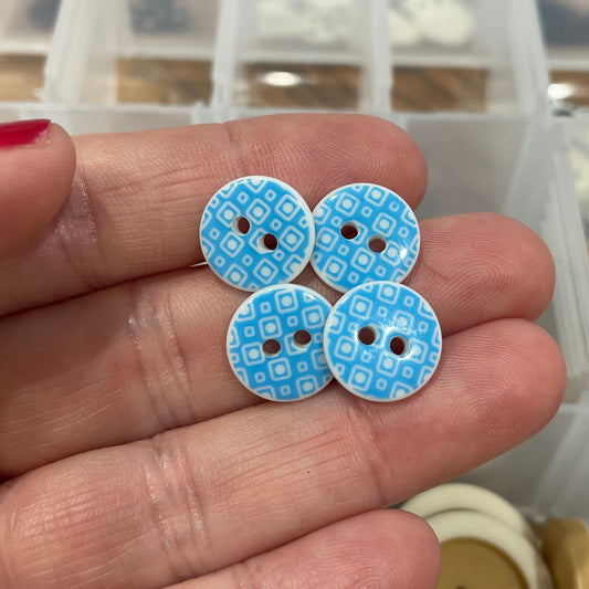 Hand holding blue decorative buttons with a button collection container in the background