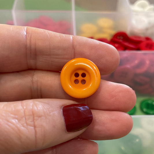 Hand holding a yellow button with a container of colorful buttons in the background
