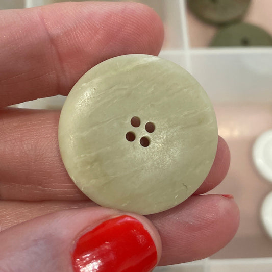 Hand holding a light-colored button with a blurred background of button collection