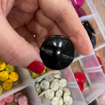 Hand holding a black button with a background of various buttons in containers