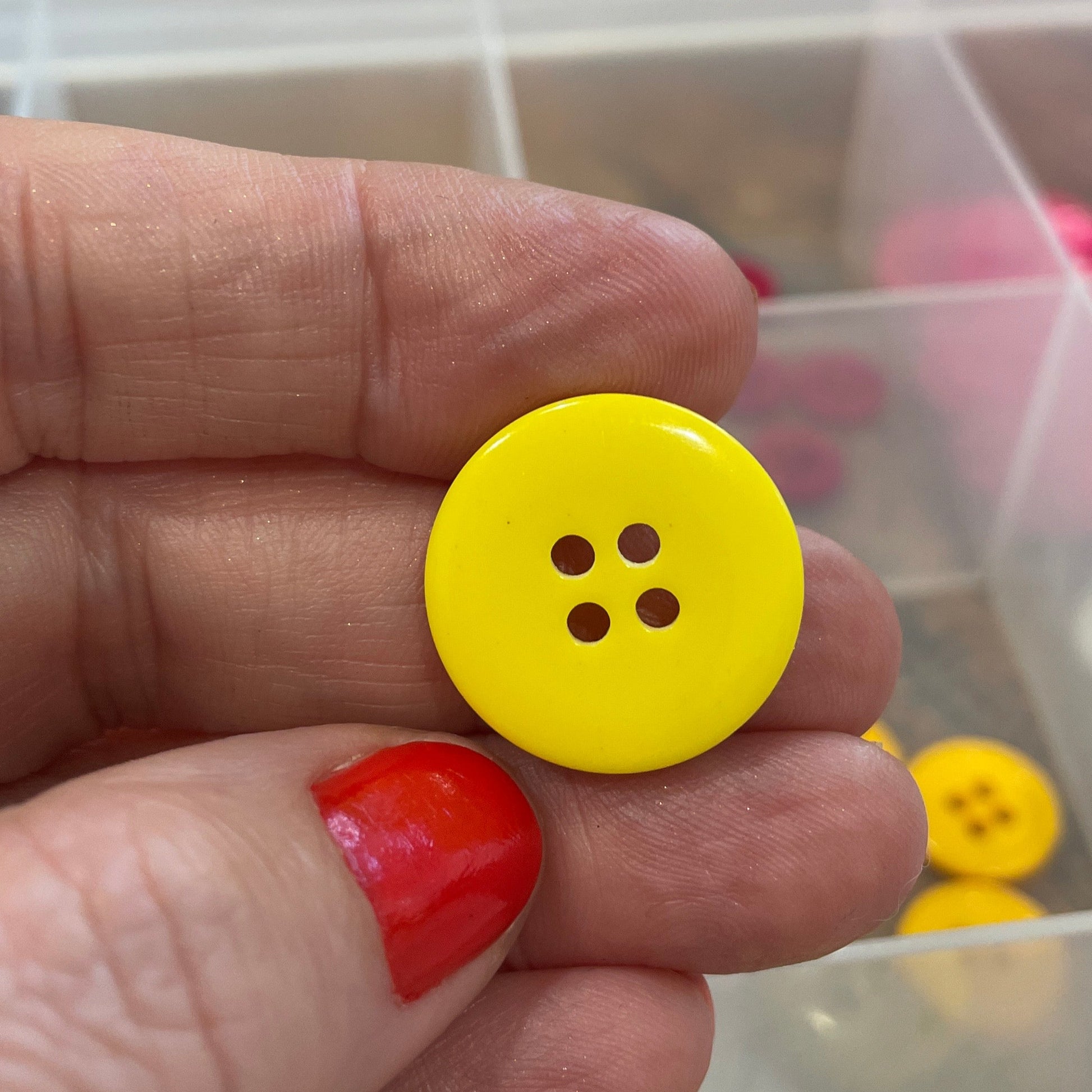 Hand holding a yellow button with a clear container of buttons in the background