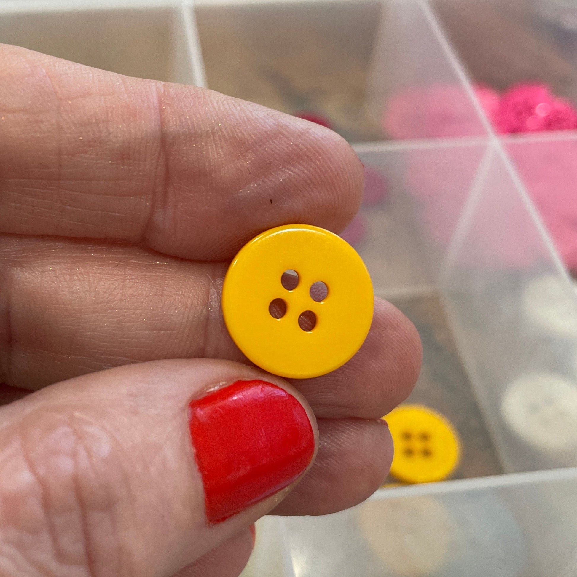 Hand holding a yellow button with a clear container of buttons in the background