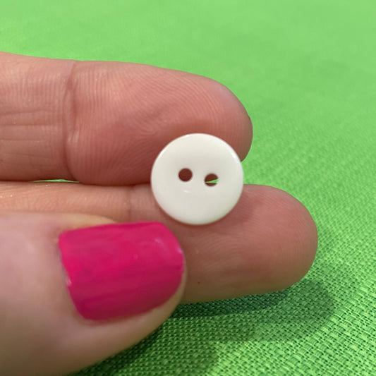 White button held between fingers against a green fabric background