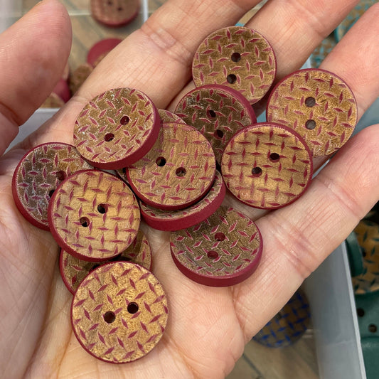 Hand holding a collection of wooden buttons with a clear container of more buttons in the background.