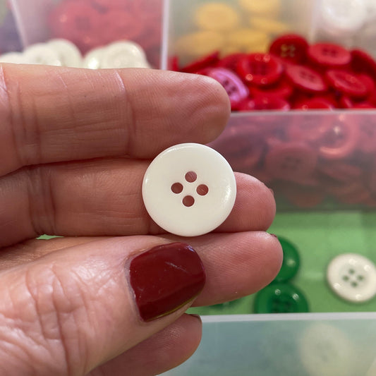 Hand holding a white button with three holes in front of a container of colorful buttons.