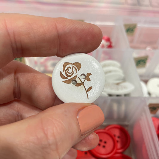 Hand holding a white button with a rose design against a background of various buttons.