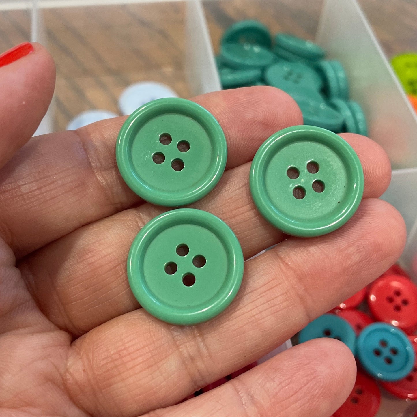 Green buttons held in a hand with a container of buttons in the background