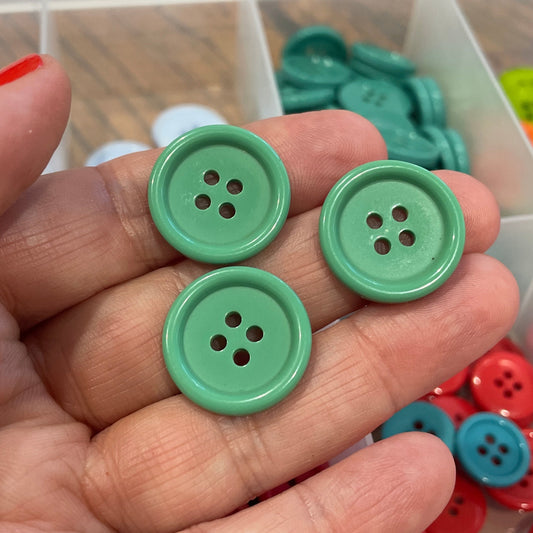Green buttons held in a hand with a container of buttons in the background