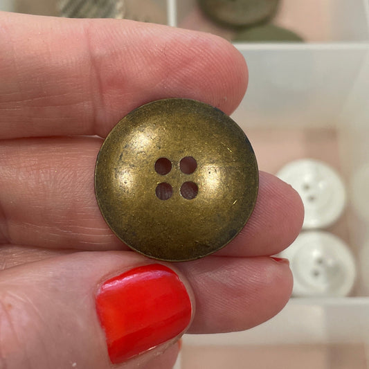 Hand holding a gold button with a background of button assortment