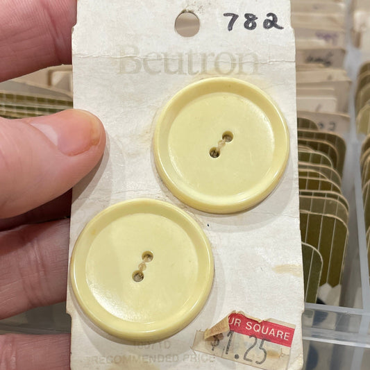 Hand holding a card with two yellow buttons against a blurred background of a storage box.