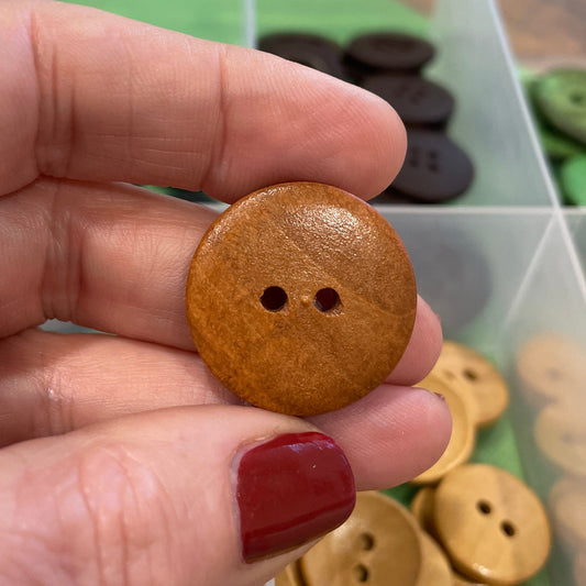 Wooden button held by a hand with a container of buttons in the background