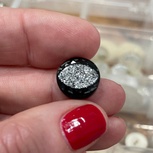 Hand holding a black and silver earring with red nail polish, against a background of jewelry boxes.