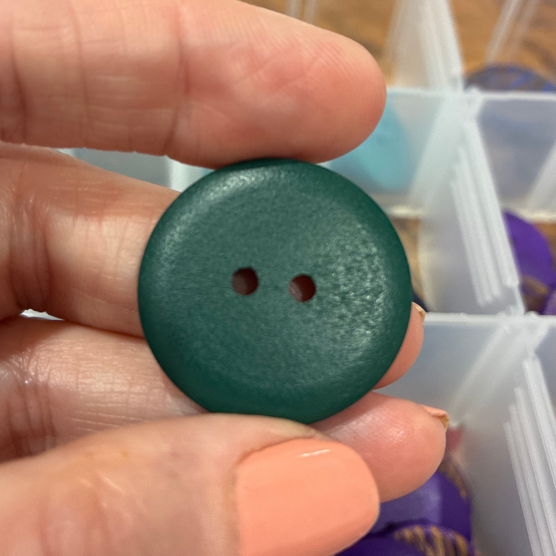 Green button held between fingers with a container of buttons in the background