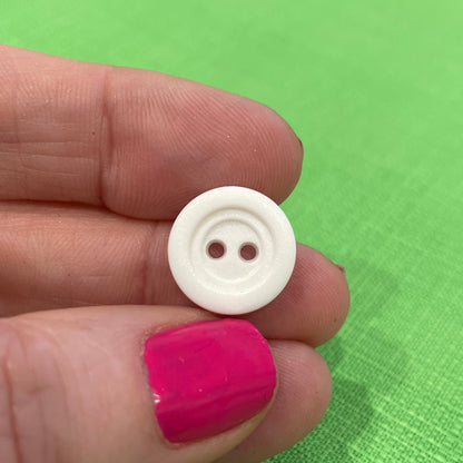 White button held between fingers against a green background