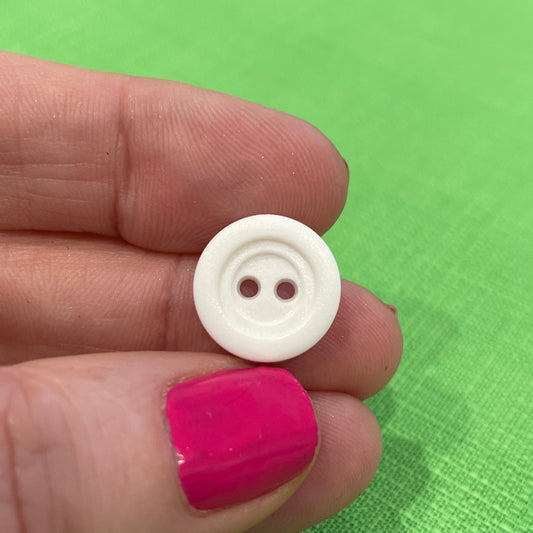 White button held between fingers against a green background