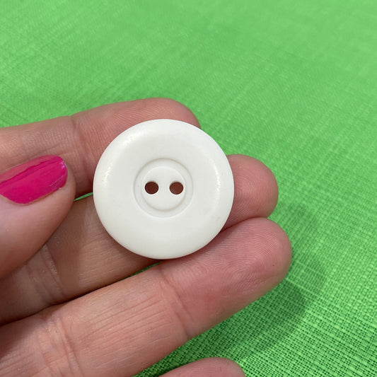 White button held between fingers against a green fabric background