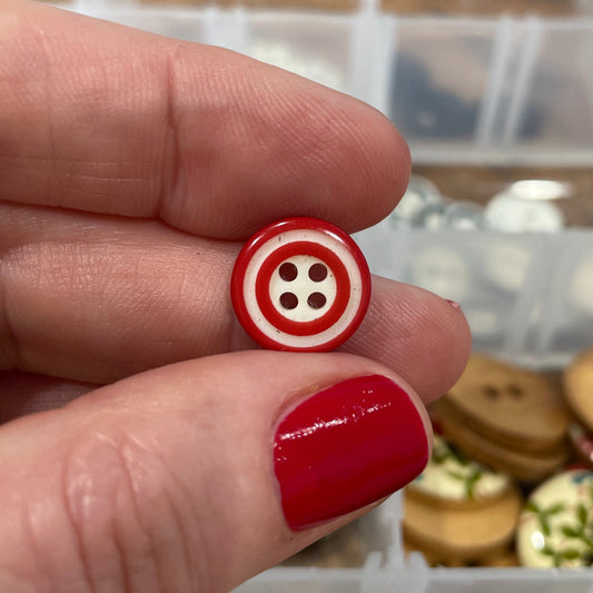 Hand holding a red and white button with a blurred background of a button collection.